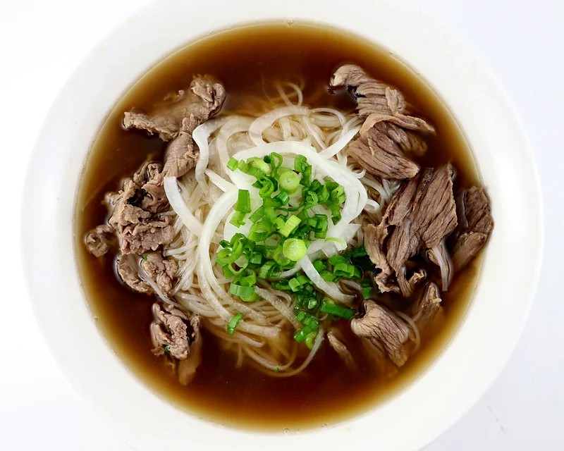 Bowl of beef pho with rare steak and brisket slices, rice noodles, onion and green onion